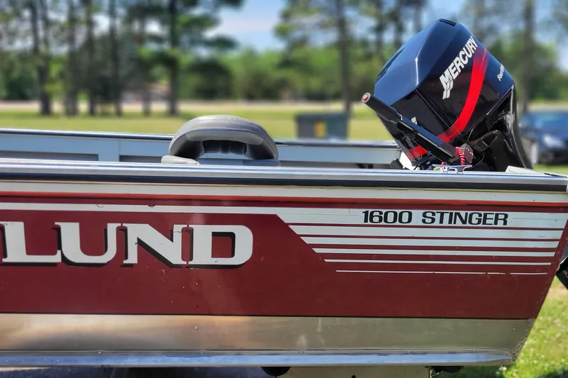 Slide: The Image of 1989 Lund 1600 Stinger boat with Mercury outboard motor, parked outdoors. - 2
