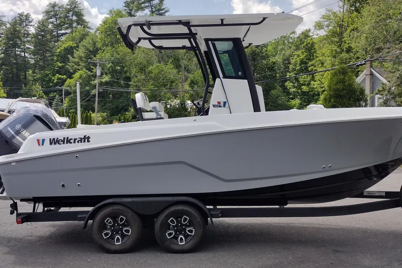 Slide: The Image of 2024 Wellcraft 223 Fisherman boat on trailer, side view, outdoors with trees in background. - 4