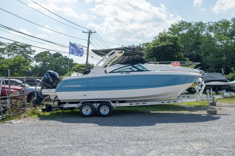 Slide: The Image of 2026 Chaparral 250 OSX boat on trailer, blue and white, for sale in outdoor lot. - 2