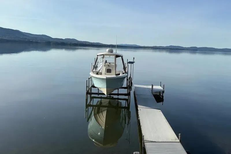 Slide: The Image of 2020 Cobia 240 Center Console boat docked on calm lake with scenic mountain backdrop. - 16