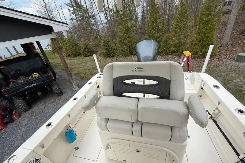 Slide: The Image of 2020 Cobia 240 Center Console boat with cushioned seating, parked near a wooded area. - 24