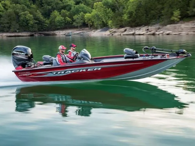 The Image of A red Tracker boat speeds across calm water, surrounded by green trees. - 1