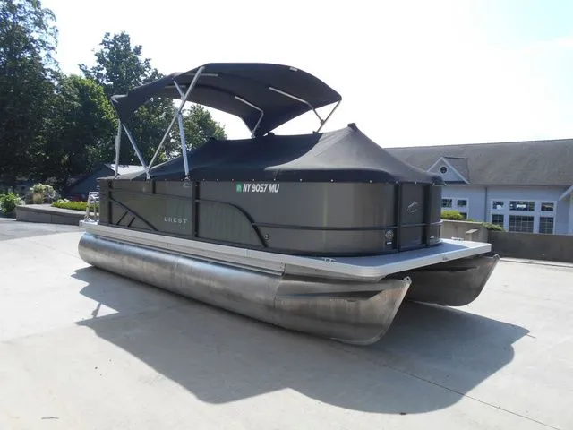 Slide: The Image of A 2024 Crest Classic LX 200 L pontoon boat with a black canopy, parked on a concrete lot. - 5
