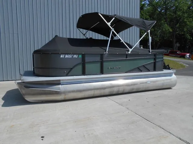 The Image of A 2024 Crest Classic LX 200 L pontoon boat with a black canopy, parked on concrete. - 1
