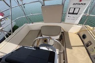 Slide: The Image of 1990 Island Packet 27 sailboat cockpit with seating and steering wheel, docked on calm water. - 3