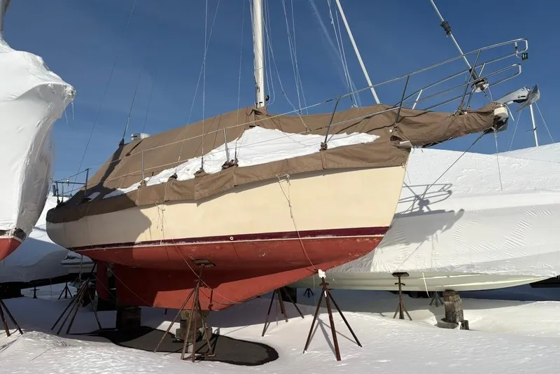 Slide: The Image of 1990 Island Packet 27 sailboat covered in snow, stored on stands outdoors. - 3