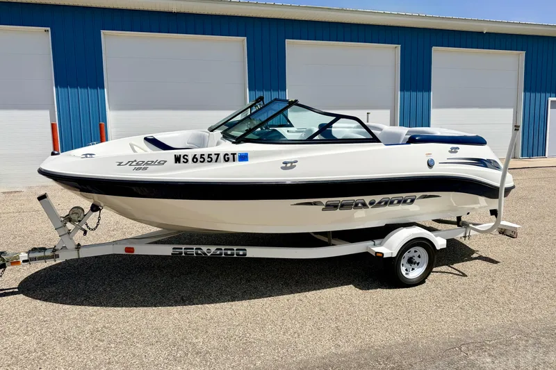 Slide: The Image of 2004 Bombardier SEADOO Utopia 185 boat on trailer, parked outside blue building. - 1