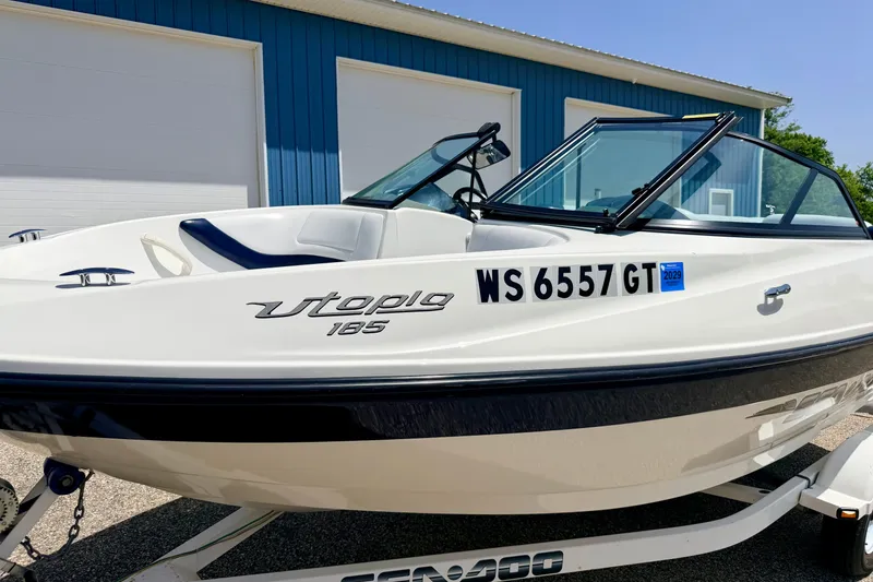 Slide: The Image of 2004 Bombardier SEADOO Utopia 185 boat on trailer, parked near blue building. - 5