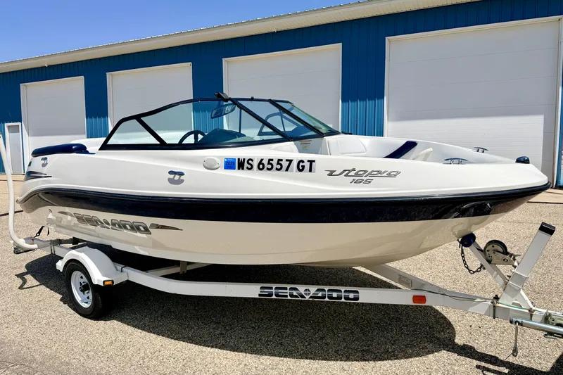 Slide: The Image of 2004 Bombardier SEADOO Utopia 185 boat on trailer, parked outside blue building. - 2