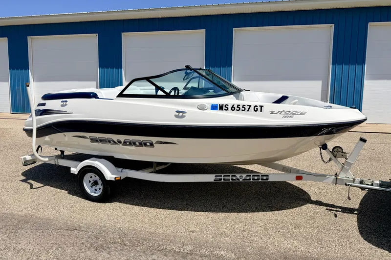 The Image of 2004 Bombardier SEADOO Utopia 185 boat on trailer, parked near blue storage units. - 0