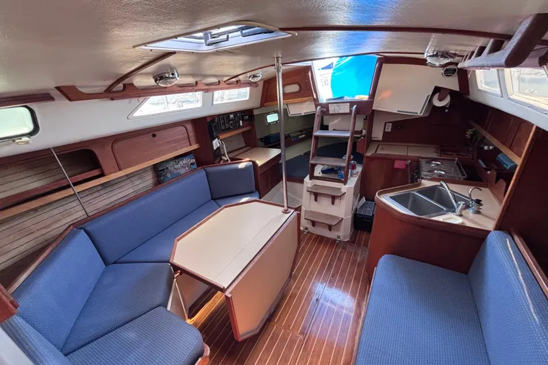 Slide: The Image of Interior of a 1989 CAL 33 sailboat with blue seating, wooden flooring, and compact kitchen. - 12