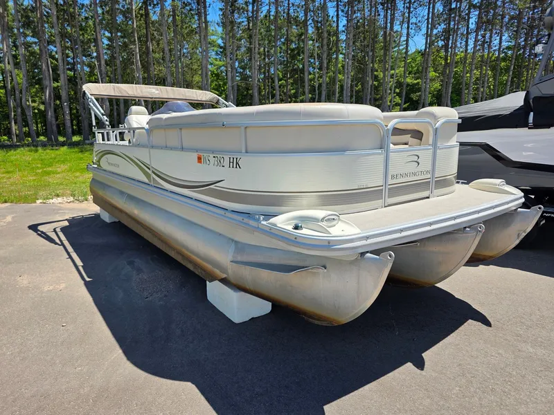 The Image of A 2008 Bennington pontoon boat is parked on a lot, surrounded by trees. - 1