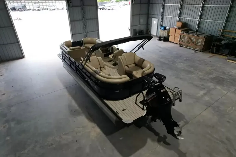 Slide: The Image of A 2019 Silver Wave 230 Island CLS pontoon boat in a warehouse. It features beige seating and an outboard motor. - 12