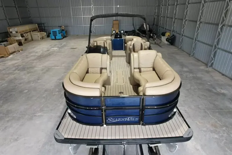 Slide: The Image of A 2019 Silver Wave 230 Island CLS pontoon boat in a warehouse, featuring beige seating and blue paneling. - 20