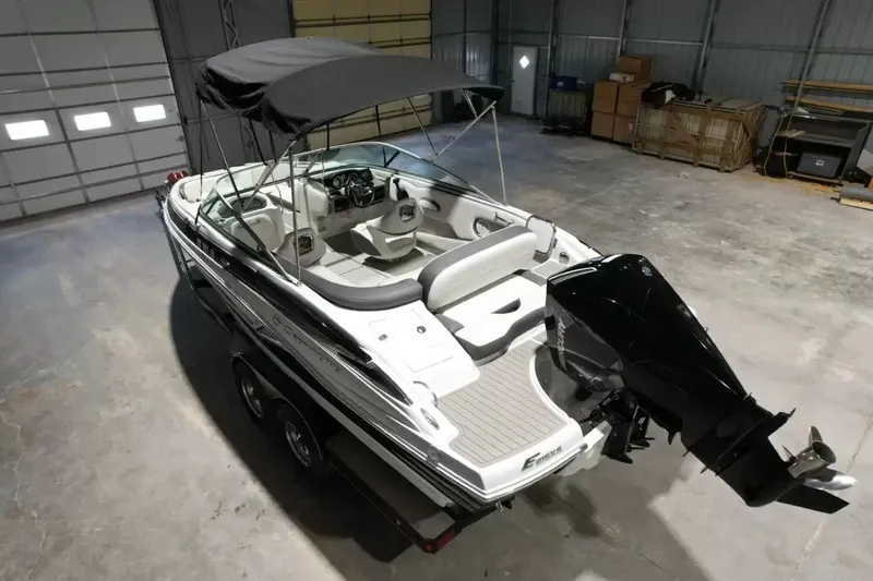 Slide: The Image of A 2021 Crownline Eclipse E215 XS boat in a warehouse. It features a black canopy and outboard motor. - 10