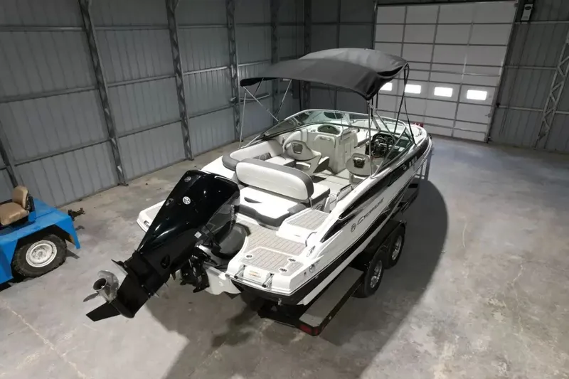 Slide: The Image of A 2021 Crownline Eclipse E215 XS boat is in a warehouse. It features a black canopy. - 6