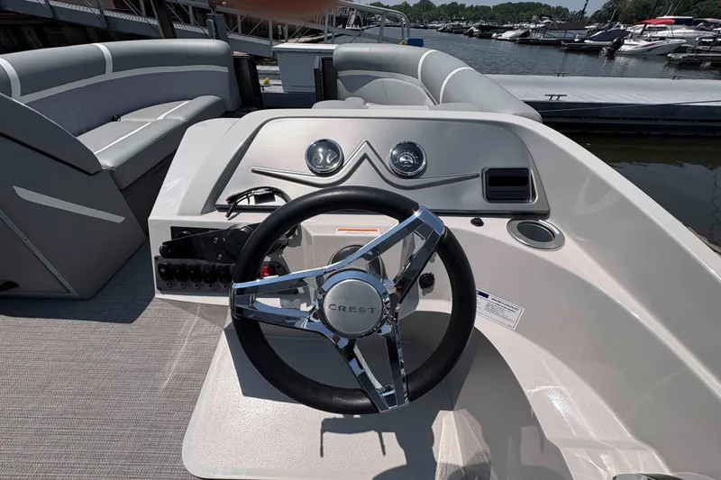 Slide: The Image of 2023 Crest Classic DLX 220 boat interior with steering wheel and seating, docked at marina. - 12