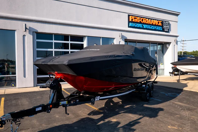 Slide: The Image of 2027 MasterCraft XT24 boat covered, parked outside Performance Marine Watersports dealership. - 15