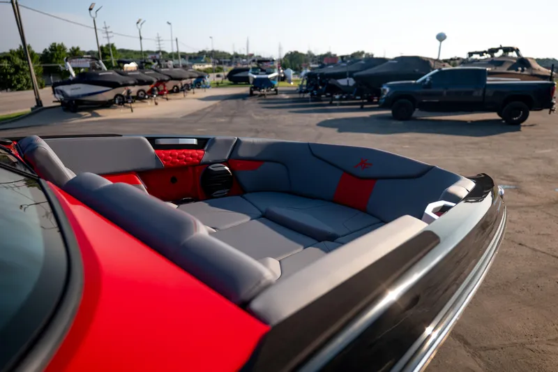 Slide: The Image of 2027 MasterCraft XT24 boat interior with red and gray seating, parked outdoors. - 38