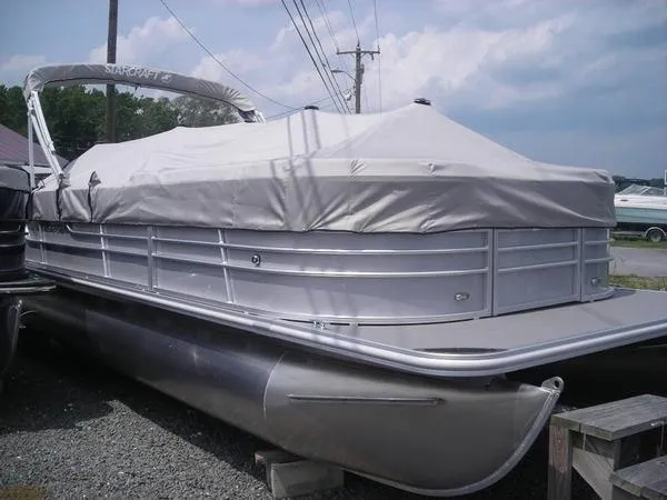 Slide: The Image of A 2017 Starcraft EX 23 C pontoon boat with a gray cover, parked on a gravel lot. - 1