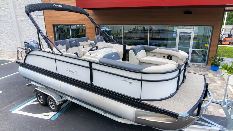 Slide: The Image of A sleek 2026 Barletta SANZA 22UC pontoon boat on a trailer, parked outside a modern building. - 3