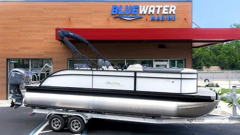 Slide: The Image of A 2026 Barletta SANZA 22UC pontoon boat on a trailer in front of a Bluewater Marine building. - 23