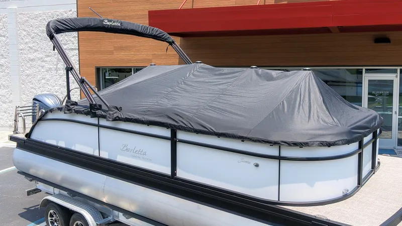 Slide: The Image of A 2026 Barletta SANZA 22UC pontoon boat with a cover, sitting on a trailer. - 2