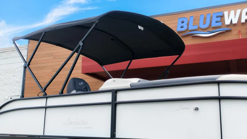 Slide: The Image of The image shows a Barletta SANZA 22UC boat with a black canopy in front of a building. - 22