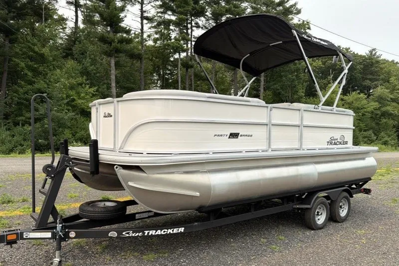 The Image of 2026 Sun Tracker Party Barge 20 DLX pontoon boat on trailer, parked in wooded area. - 0