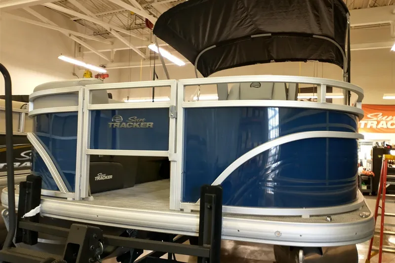 Slide: The Image of 2026 Sun Tracker SportFish 20 DLX pontoon boat in showroom, featuring blue exterior and canopy. - 3