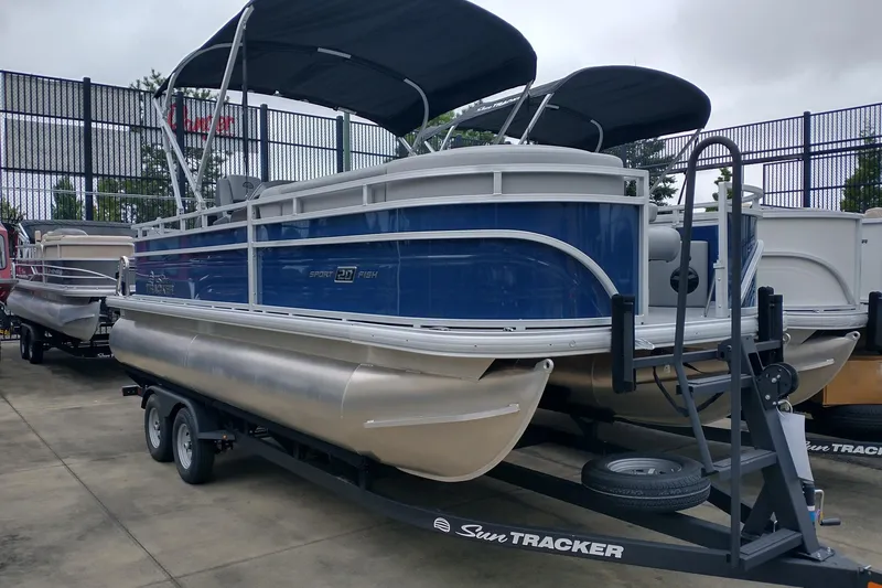The Image of 2026 Sun Tracker SportFish 20 DLX pontoon boat on trailer, blue and silver design. - 0