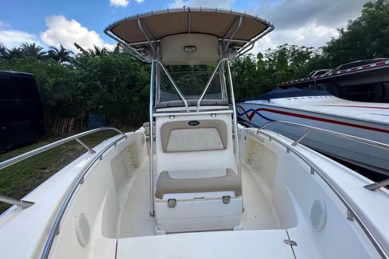 Slide: The Image of 2012 Scout 225 XSF boat with T-top, parked outdoors, surrounded by greenery. - 6