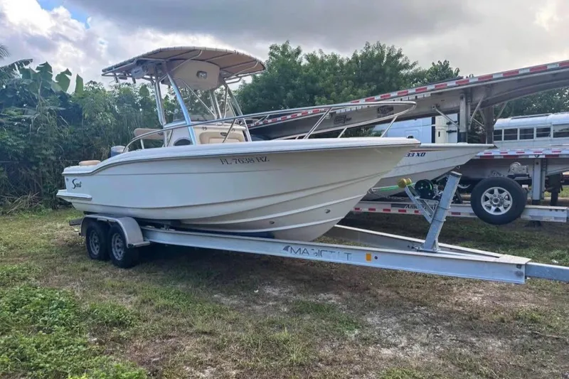 The Image of 2012 Scout 225 XSF boat on trailer, parked outdoors with lush greenery background. - 1