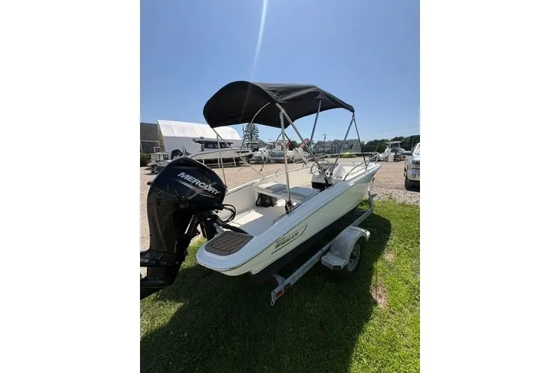 Slide: The Image of 2024 Boston Whaler 130 Super Sport boat with canopy on trailer, sunny day. - 2