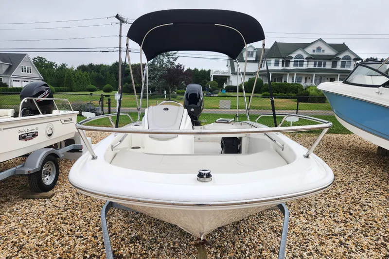Slide: The Image of 2024 Boston Whaler 130 Super Sport boat with canopy, parked on gravel near houses. - 8