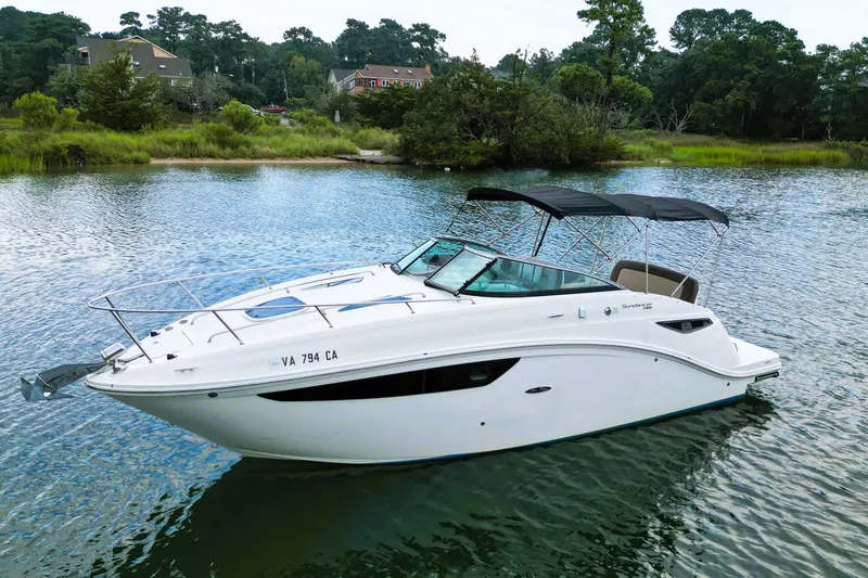 The Image of 2015 Sea Ray Sundancer 260 boat on calm water, surrounded by lush greenery. - 0