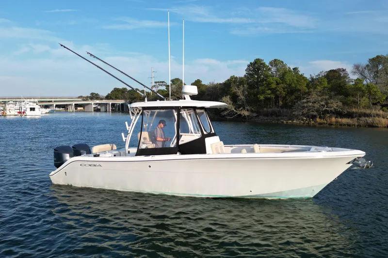 The Image of 2016 Cobia 296 Center Console boat on calm water, with fishing rods and scenic background. - 0
