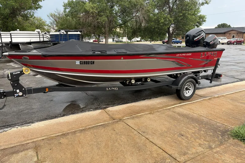Slide: The Image of 2024 Lund 1875 Pro Guide boat on trailer, parked outdoors with cover. - 0