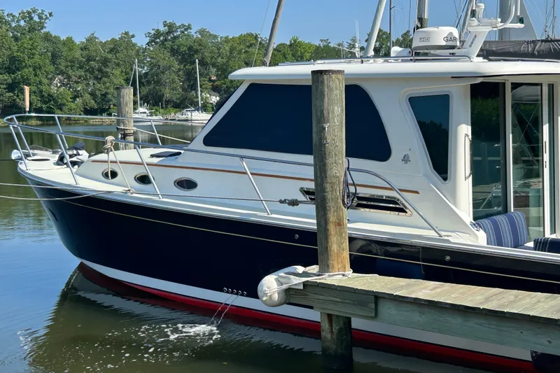 The Image of 2016 Back Cove 34 boat docked on calm water, surrounded by lush greenery. - 2
