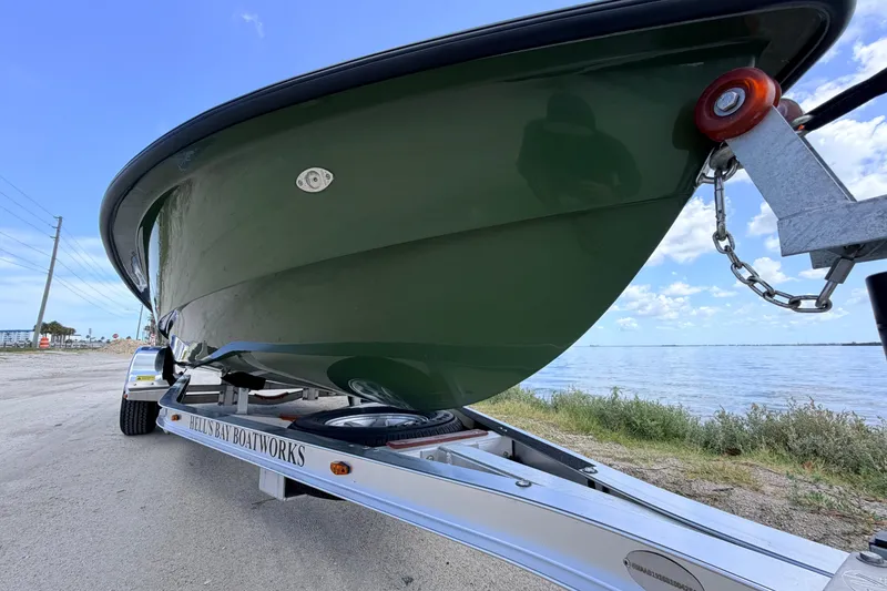 Slide: The Image of 2025 Hell's Bay Professional boat on trailer by waterfront, showcasing sleek green hull design. - 9