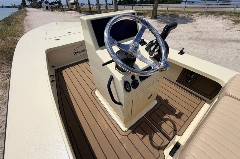 Slide: The Image of 2025 Hell's Bay Professional boat interior with steering wheel and console, docked by a sandy path. - 44
