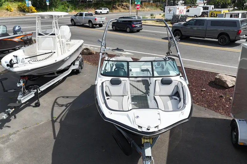 Slide: The Image of 2016 Yamaha Boats 212X on trailer, parked beside another boat, with street view in background. - 15