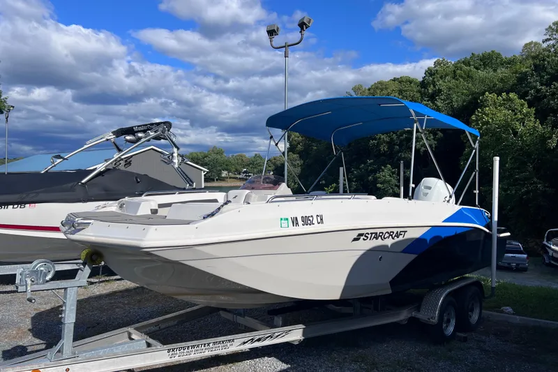 Slide: The Image of 2021 Starcraft SVX 211 OB boat on trailer with blue canopy, parked outdoors. - 2