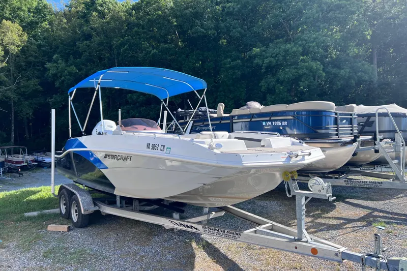The Image of 2021 Starcraft SVX 211 OB boat with blue canopy on a trailer in a marina. - 0