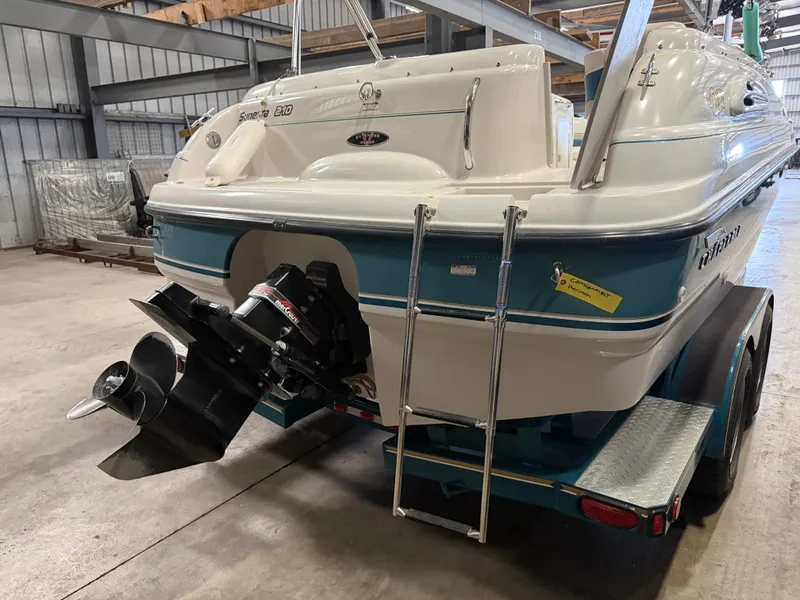 Slide: The Image of A 1996 Chaparral 210 Sunesta in a warehouse. It features an outboard motor and a ladder. - 12