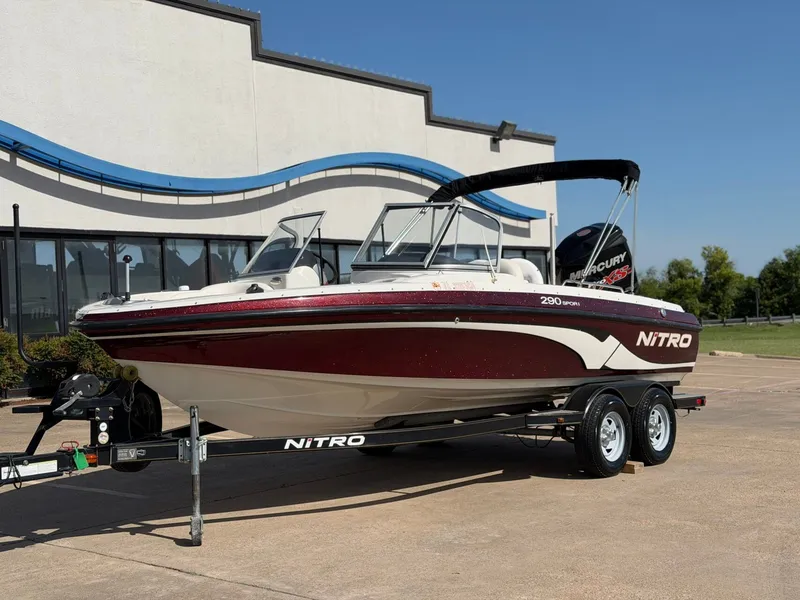 Slide: The Image of A 2013 Nitro 290 Sport boat on a trailer, parked in front of a modern building. - 2