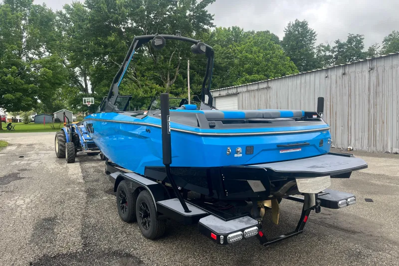Slide: The Image of 2026 Axis A225 boat in vibrant blue on a trailer, parked outdoors near trees and a shed. - 7