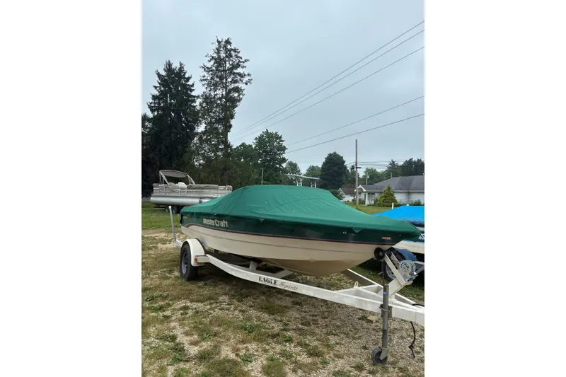 The Image of 1996 MasterCraft ProStar 190 boat with green cover on trailer, parked outdoors. - 0