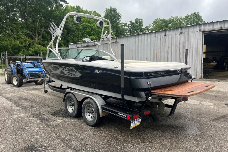 Slide: The Image of 2004 MasterCraft X-9 boat on trailer, parked near a metal building and tractor. - 3