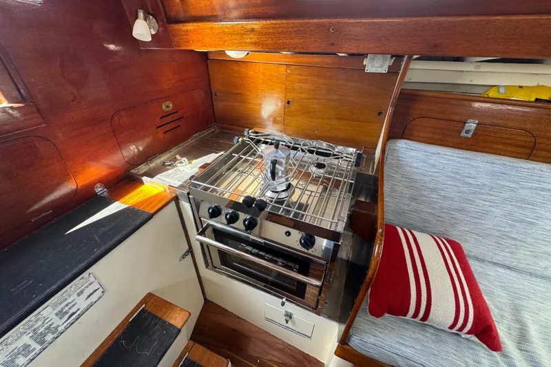 Slide: The Image of 1955 Henry R Hinckley Owens Cutter interior with stove, wooden cabinetry, and striped cushion. - 12